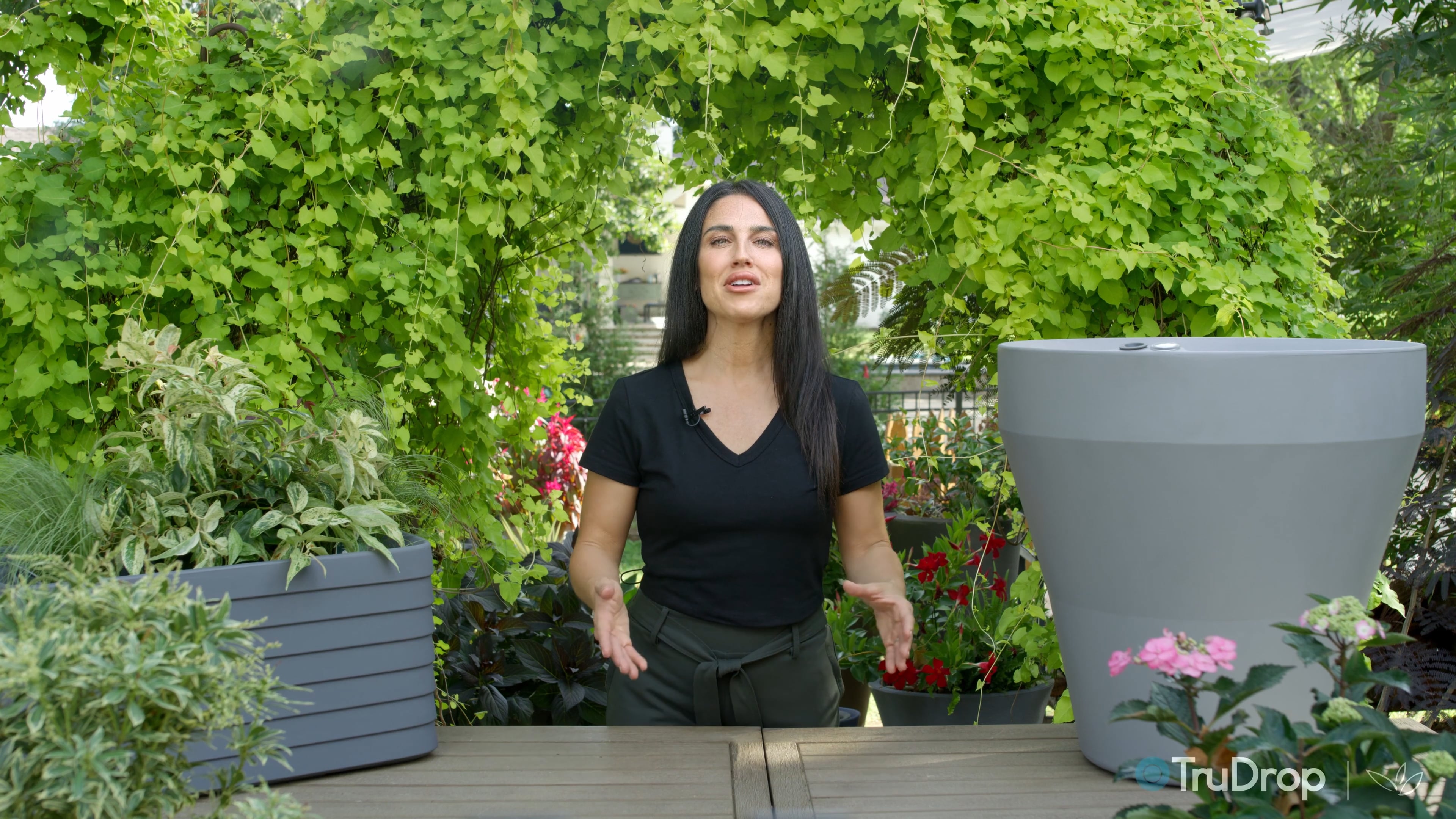 Woman presenting TruDrop self-watering planters on a garden deck with lush green backdrop