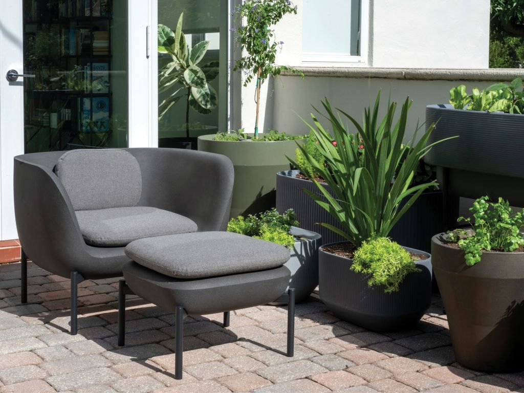 Crescent Garden InOu Elements Arm Chair and Ottoman with a variety of Crescent Garden planters in the background.